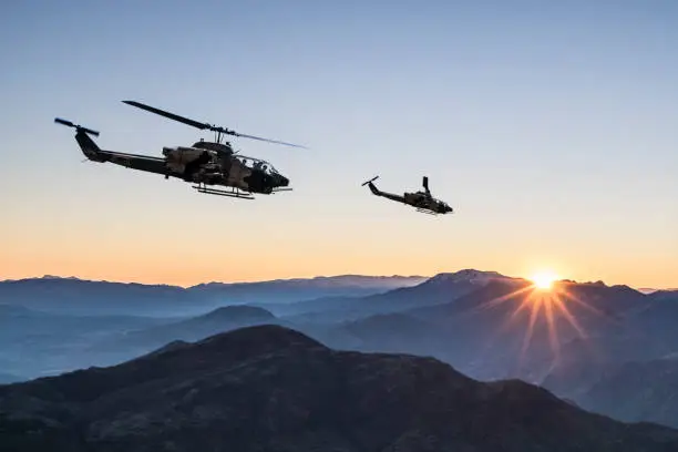 Photo of AH-1 Cobra Attack helicopters flying over mountains at sunrise