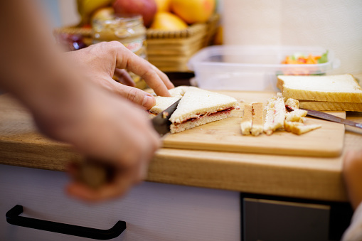 Close-up of unrecognizable father making peanut butter and jelly crustless sandwiches for his son