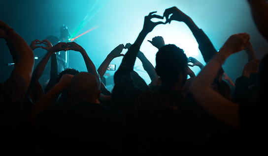 Rearview shot of unrecognizable people making heart shapes during a concert  in a nightclub