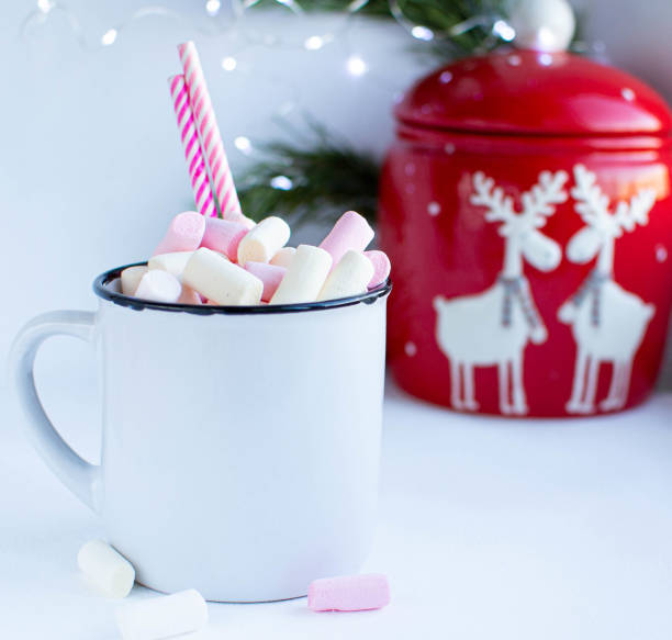 istock a white cup with marshmallows and Christmas sweets, on a white background with fir branches, balls and Christmas lights, as well as with a large red jar with deers in the background 1195008984