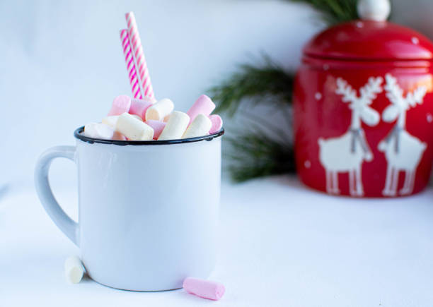 istock a white cup with marshmallows and Christmas sweets, on a white background with fir branches, balls and Christmas lights, as well as with a large red jar with deers in the background 1195009598