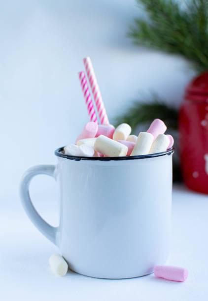 istock a white cup with marshmallows and Christmas sweets, on a white background with fir branches, balls and Christmas lights, as well as with a large red jar with deers in the background 1195009606