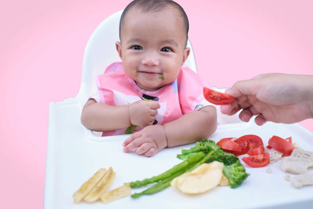 手で食べるかわいいアジアの女の子、blw法で有機野菜を食べる小さな赤ちゃん、赤ちゃんが泣き出し、 - baby chicken 写真 ストックフォトと画像