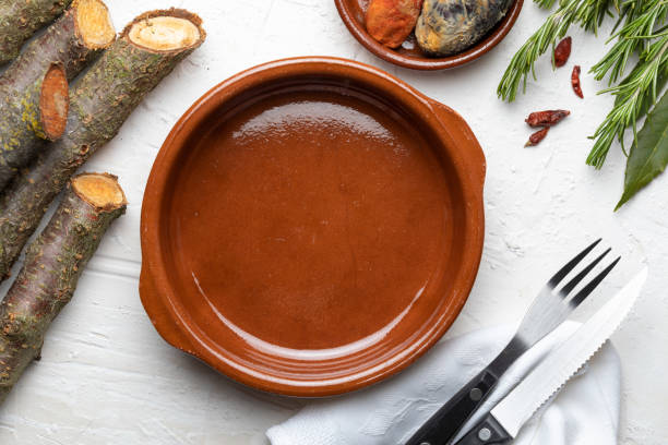 olla de barro vacía. sobre fondo de madera blanca. de aspecto rústico incluye especias (romero, laurel, chiles) y cubiertos. concepto para incluir su comida y su texto. - terra cotta pot fotografías e imágenes de stock