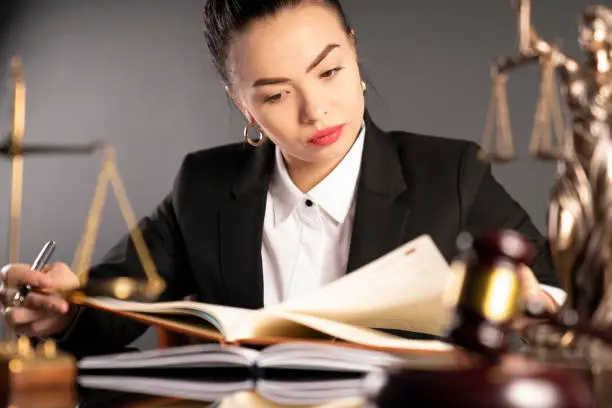 Young lawyer during work in chamber. Gavel, scale and Themis statue on the table.