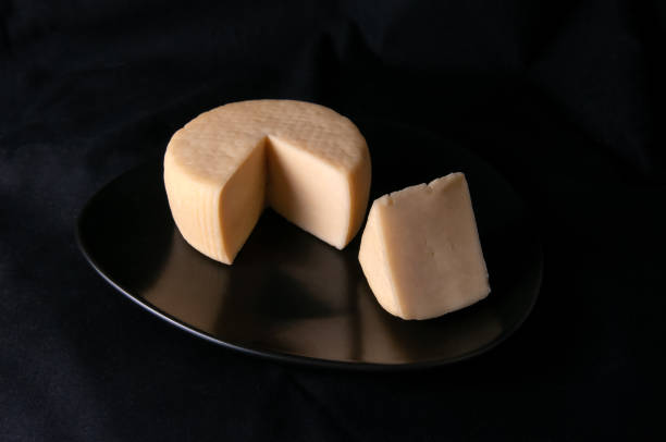 istock Caciotta cheese on a black plate. A piece of triangular shape is cut off from the cheese. Black background. Isolated. Close-up 1195014581