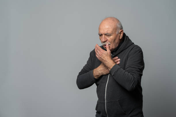 Senior man coughing into his hand, isolated on white background stock photo