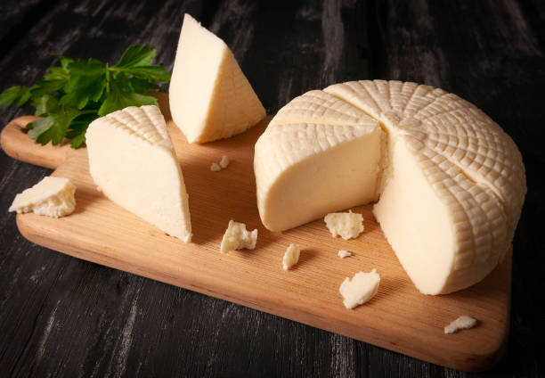 istock Suluguni cheese is cut into large pieces. On a light wooden board. Decorated with greenery. Dark wooden background 1195014832