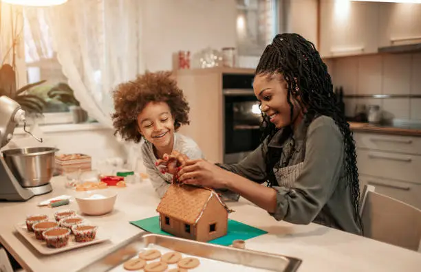 Cute 5 years old girl and her mom assemble gingerbread house for Christmas.