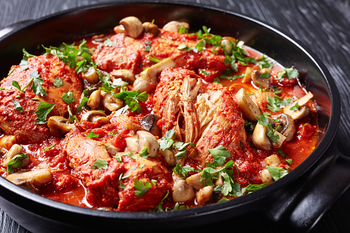 close-up of Chicken Cacciatore with tender chicken breasts, tomatoes, bell peppers, carrots and sliced mushrooms in a black ceramic dutch oven