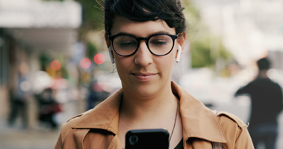 Cropped shot of an attractive young businesswoman using a smartphone while swearing ear pods in the city during the day