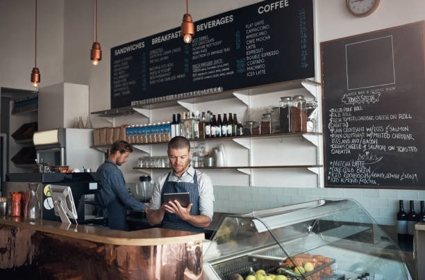 Tracking tasks on his digital device Shot of a mature man using a digital tablet while working alongside a colleague in a cafe cafe tablet stock pictures, royalty-free photos & images