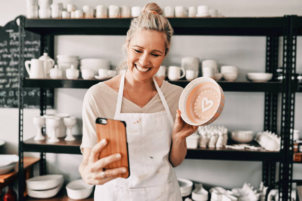 Hey, look guys! Cropped shot of an attractive mature woman using her cellphone to take a selfie with her pottery in her studio pottery photos stock pictures, royalty-free photos & images
