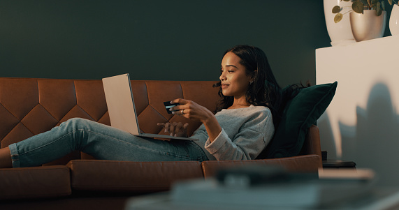 Shot of an attractive young woman using her credit card and laptop to shop online while relaxing at home