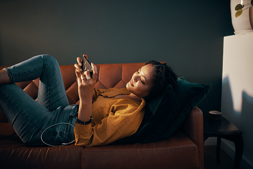 Shot of an attractive young woman using her cellphone while relaxing on a sofa at home