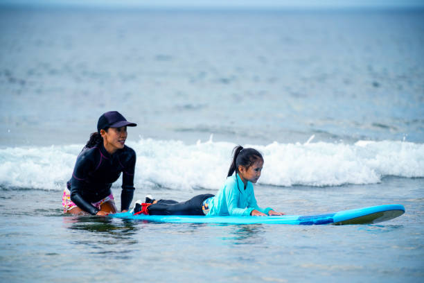 istock Mother teaching her young daughter how to surf during a tropical vacation 1195045800