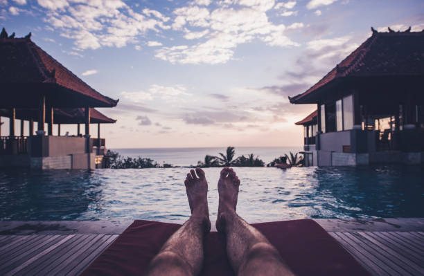 A man's feet lying on the mattress on a wooden platform under a blue sky