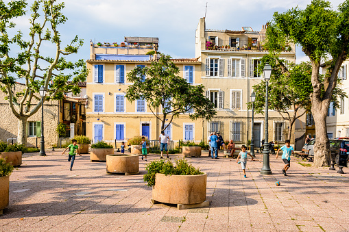 Marseille, France - May 20, 2018: Late in the afternoon children play football between flower boxes on the place des Moulins in the historic district of Le Panier, while elders chat together.