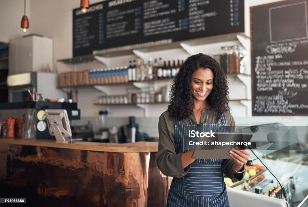 Technology allows me to simplify all my business operations Shot of a young woman using a digital tablet while working in a cafe Owner Stock Photo