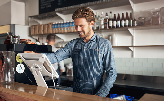 Shot of a young waiter working on a till in a cafe