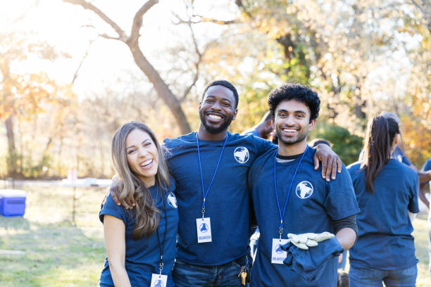 istock Three volunteers with arms around each other smile for camera 1195063221