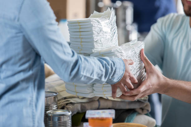 Woman donates diapers during clothing drive During a charity event, an unrecognizable woman donates a large stack of disposable diapers. A male volunteer receives the donation. adult diaper stock pictures, royalty-free photos & images