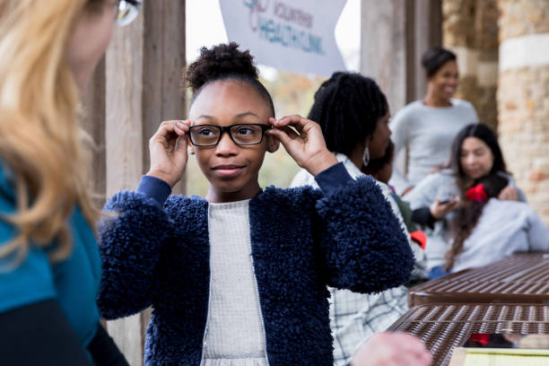 Little girl tries on glasses at outdoor free clinic Pretty preteen girl tries on a pair of stylish eyeglasses while visiting a free outdoor clinic. toll free stock pictures, royalty-free photos & images