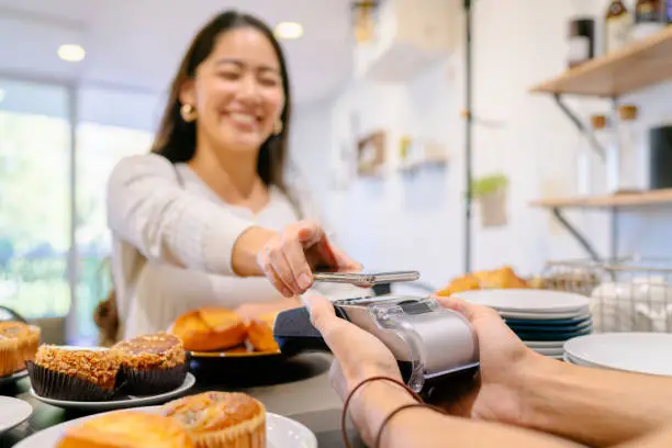 A female costumer is making a contactless payment in a cafe.