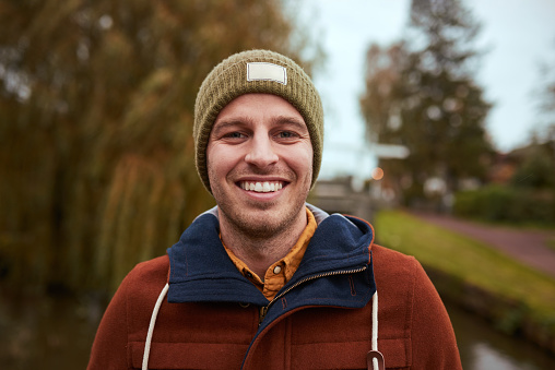 Cropped portrait of a handsome young man smiling while standing in a park in late autumn