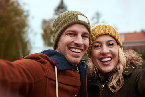 Cropped portrait of an affectionate young couple taking a selfie together while standing in a park in late autumn