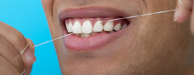 Close-up male mouth while flossing teeth with dental floss on blue background. Dental hygiene
