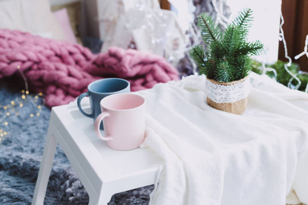 istock two pastel-colored mugs on a small portable table with Christmas decorations 1195086234