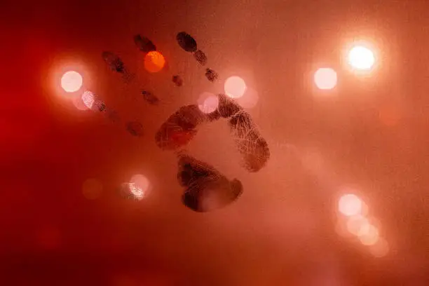 Photo of handprint on night wet glass in red colors with blurry street light in backround