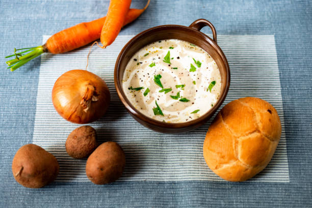 istock Creamy vegetable soup, bread and raw vegetable ingredients on table. 1195088139