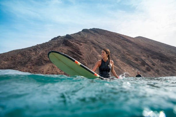 Beautiful young brunette woman surfing in fuerteventura Beautiful young brunette woman surfing in Fuerteventura in the Atlantic ocean on the background of blue sky, clouds and transparent waves breaking wave stock pictures, royalty-free photos & images