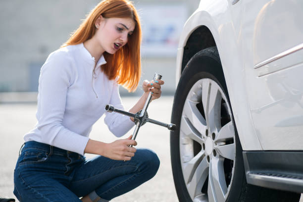istock Young woman with wrench changing wheel on a broken car. 1195098439