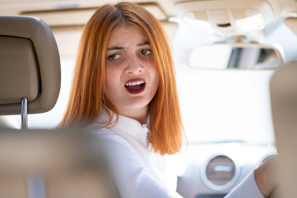 young woman driving a car backwards. girl with funny expression on her face while she made a fender bender damage to a rear vehicle. - fender bender imagens e fotografias de stock