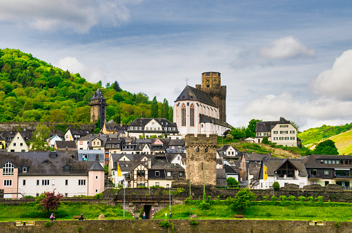 Two people ride their bicycles along the banks of the Rhine River and passing the medieval village of Oberwesel
