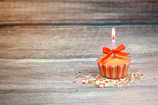 Happy birthday cupcake and bow candle on table on wooden background with copy space. Cute food happy birthday background concept