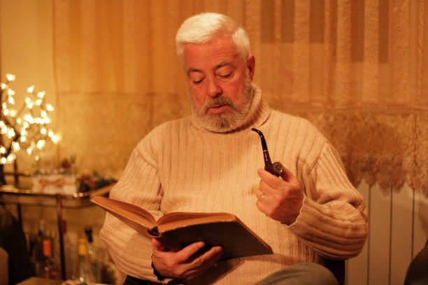 Senior man reading a book sitting on sofa at home.