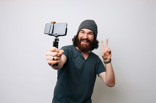 Happy amazed young bearded hipster man taking a selfie over white background