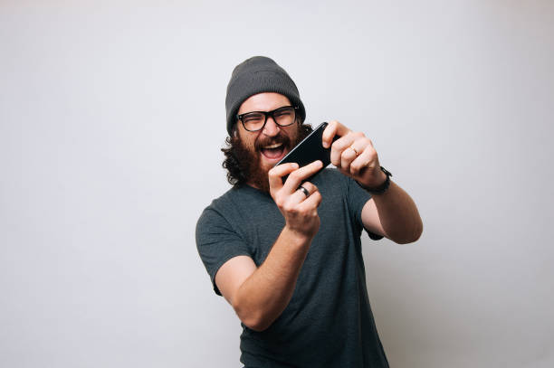 istock Happy amazed young bearded hipster man playing game on smartphone 1195118741