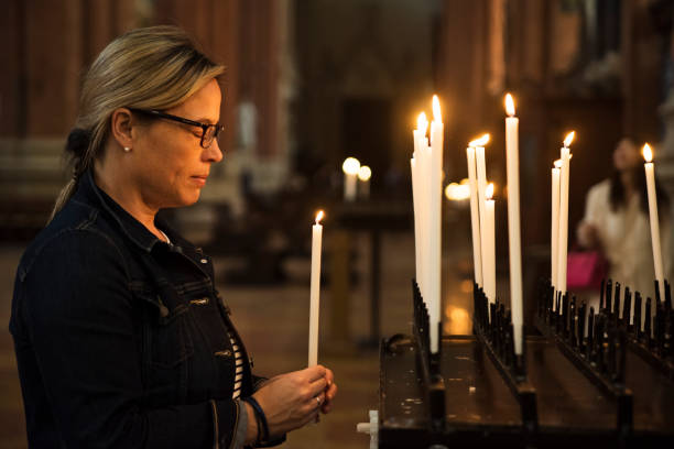 Mature woman lighting candles in church. Everyday life of freshly expatriate mature woman discovering Italy. Here she is taking time to reflect on her journey and make a wish lighting some candles in a church. Horizontal waist up outdoors shot. church ladies stock pictures, royalty-free photos & images