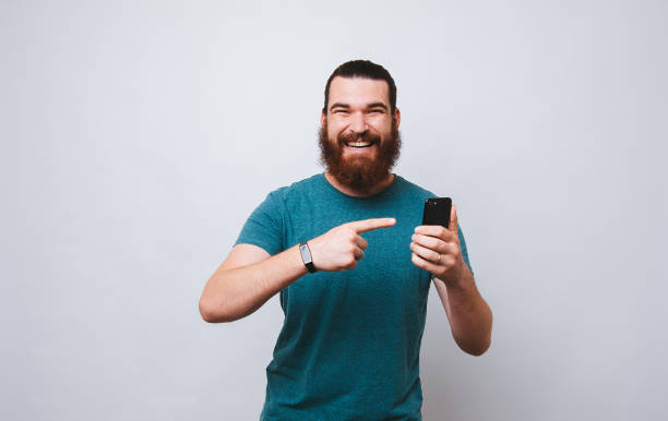 istock Happy bearded hipster man pointing at phone 1195120852