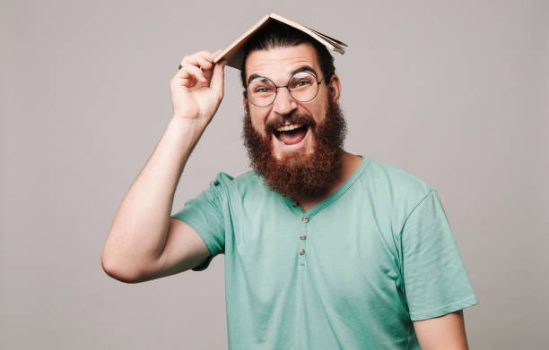 istock Happy young bearded man holding book on head 1195120878