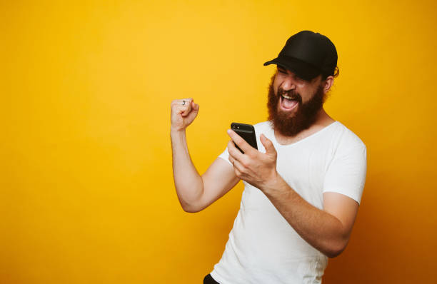 hombre barbudo feliz celebrar el éxito y mirar el teléfono - suit soccer men sport fotografías e imágenes de stock