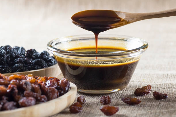 mélasse de raisin dans le bol en verre, dans la cuillère en bois et raisins noirs et verts séchés sur le fond de sac de toile de jute, nourriture saine - molasses photos et images de collection