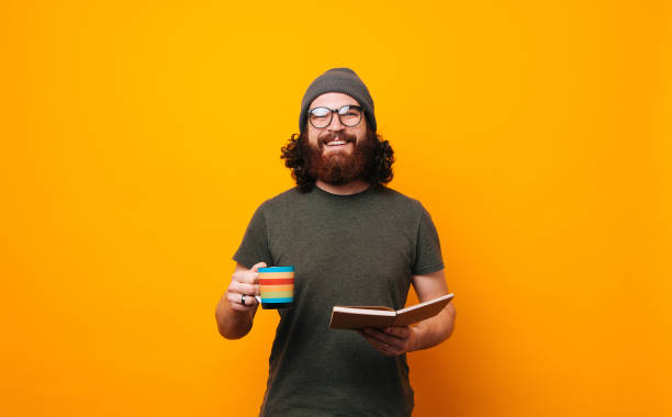 glücklicher mann mit kaffee und buch, der selbstbewusst in die kamera schaut - uncool stock-fotos und bilder