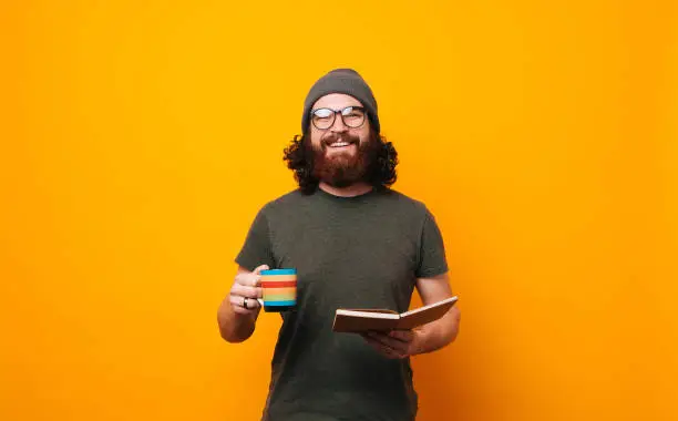 Photo of Happy man with coffee and book looking confident at the camera