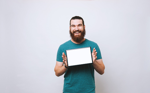 Cheerful bearded man showing blank screen on tablet